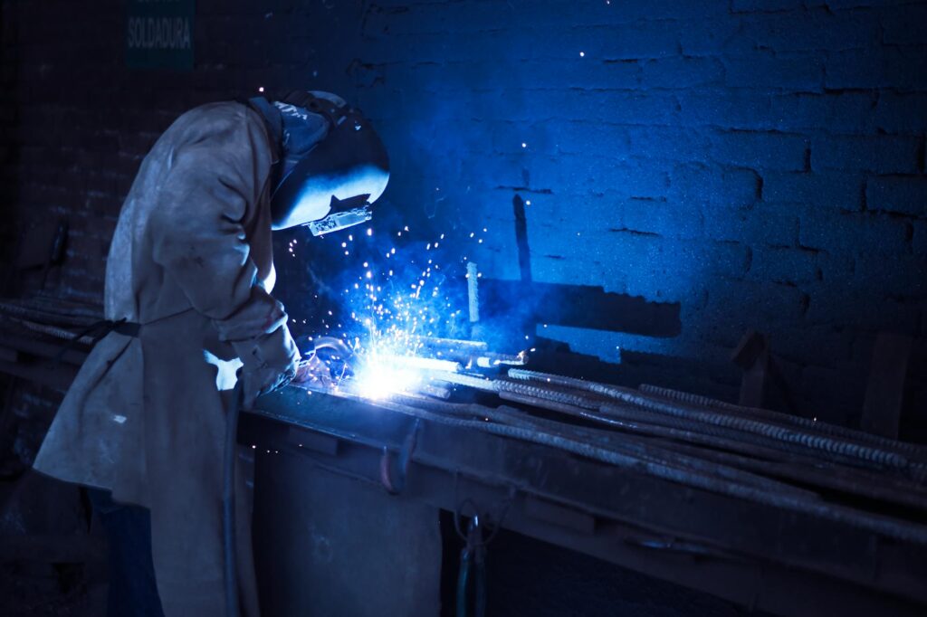 man wearing welding helmet welding metal near gray brick wall