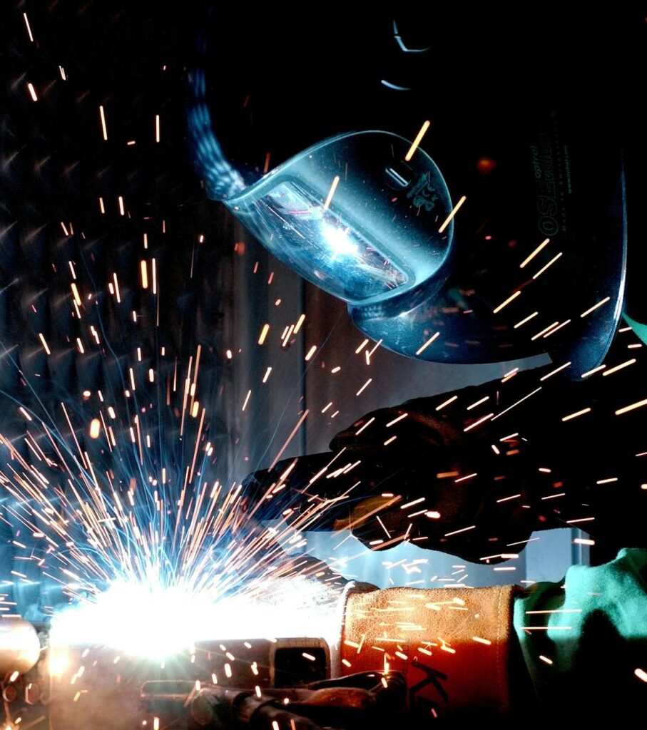 person in welding mask while welding a metal bar